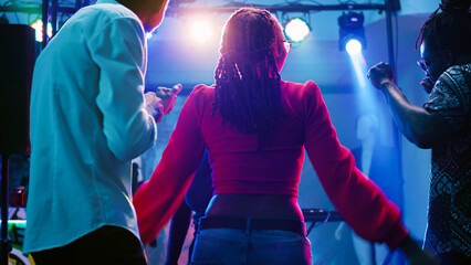 Men and women dancing at nightclub and listening to music, having fun at club with stage lights....