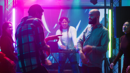 Friends enjoying funny dance battle, having fun partying together at club with electronic sounds...