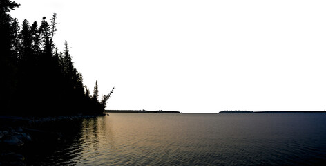 A late evening panoramic view of a calm lake with a silhouette shoreline of evergreen trees and a...