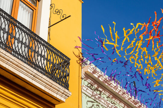 Yellow building with balcony next to papers hanging from the ceiling