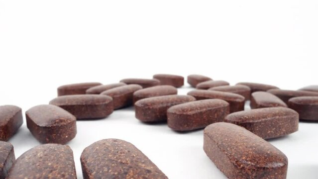 Scattered herbal supplement pills on a clean white background with a soft focus