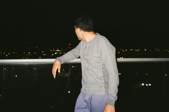 Young Man Enjoying Nighttime City View From Balcony.