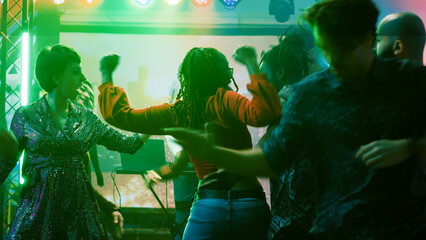 Persons having fun at dance party in nightclub, enjoying modern dance battle to show off funky moves on dance floor. Happy young adults dancing and jumping around on music mix.