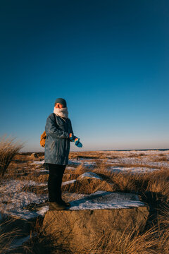 Female in Winter Clothing Standing on Rock in Sparse Snowy Field