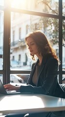 Woman in a business outfit sitting at a table and using a laptop computer with natural lighting