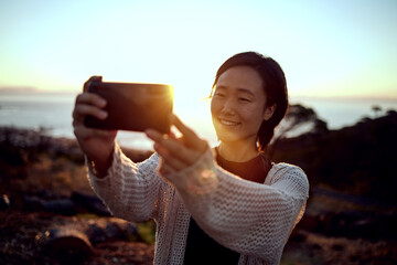 Hiking, selfie and Asian woman on mountain with sunset sky, smile and relax in nature on holiday...