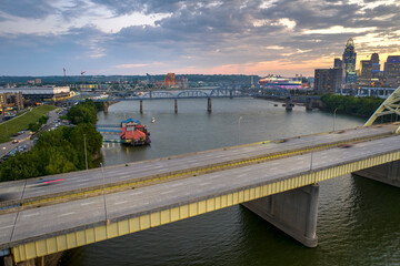 Highway traffic with driving cars on bridge in downtown district of Cincinnati city in Ohio, USA. American city skyline with brightly illuminated high commercial buildings at sunset