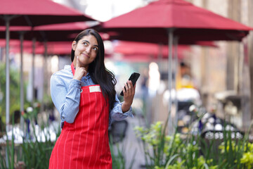 mexican woman restaurant owner thinking, holding cellular phone