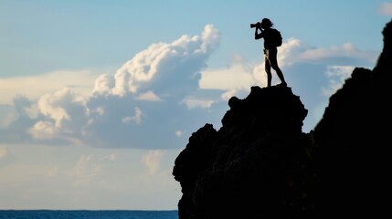 A silhouette of a person standing on a rocky cliff binoculars in hand scanning the horizon for any signs of endangered sea turtles coming ashore to lay their eggs. .