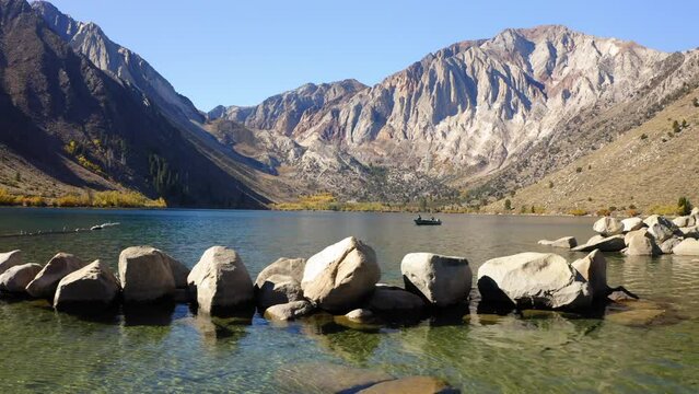 Aerial: Drone Panning Shot Of People In Nautical Vessel Moving On Convict Lake Amidst Rock Formations During Vacation - Mammoth Lakes, California
