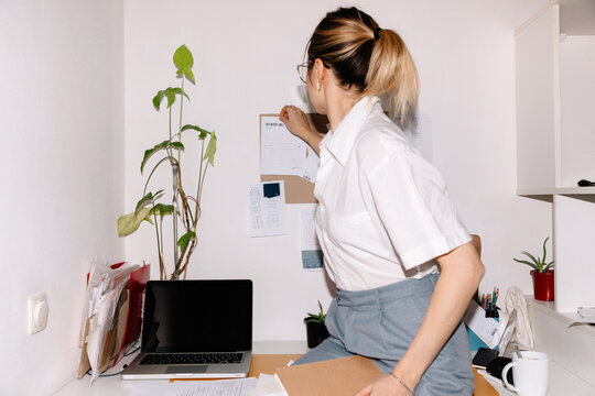 Young woman pinning papers on pinboard in office