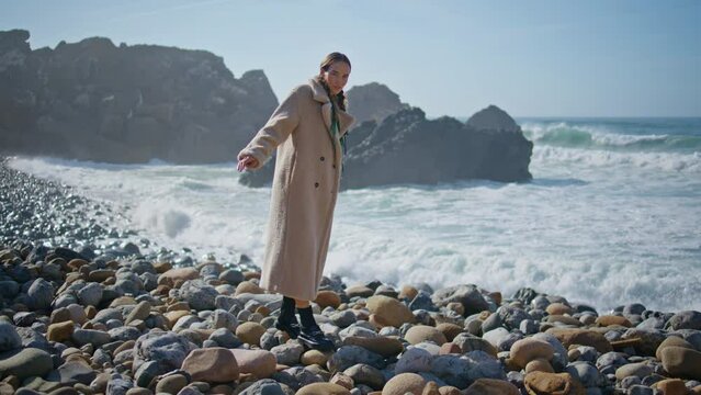 Girl walking beach stones in sunlight. Thoughtful traveler balancing rocky beach