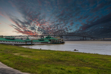 The Horace Wilkinson Bridge over the flowing waters off the Mississippi River with boats on the water, lush green grass and clouds at Louisiana Memorial Plaza in Baton Rouge Louisiana USA