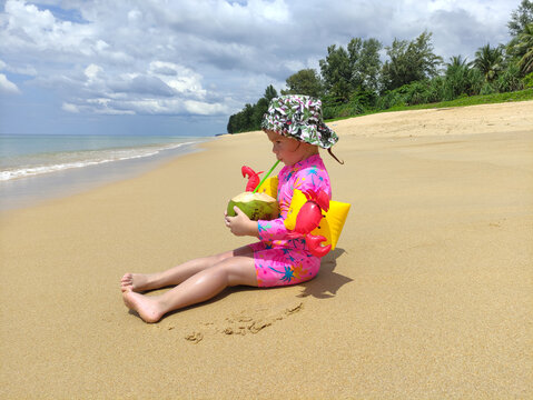 cute child enjoys coconat milk sitting onbeach sand
