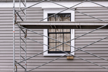 Vintage identical double hung windows and dormers on a beige color exterior wall of an old building. The windows are black with white trim. There's construction scaffolding in front of the building.