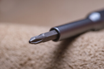 A screwdriver with a sharp point is shown on a tan surface. Concept of precision and focus, as the...