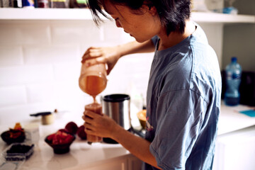 Woman, face and smoothie in kitchen with pouring for healthy breakfast, morning routine and body detox. Person, meal prep and food mixer for organic drink, wellness and vegan diet on counter in home