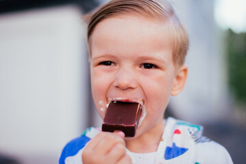 A young 4 years old boy eating icecream outside, wearing colorfull jacket and smiling