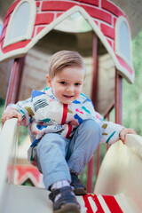 A young 4 years old boy playing at the playground outside, wearing colorfull jacket