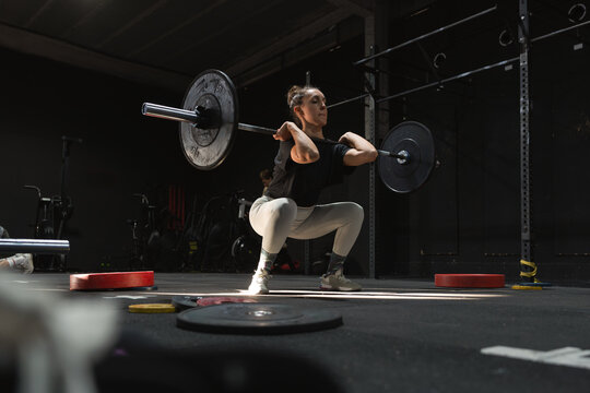 Pregnant woman performing squats with a barbell at the gym