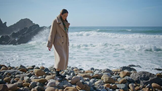 Carefree girl walking seashore stepping on beach stones. Ocean waves washing