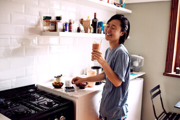 Asian woman, happy and smoothie in kitchen for healthy breakfast, morning routine and body detox in...