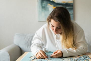 Young woman in assembling jigsaw puzzle at home
