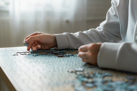 Anonymous woman in white hoody assembling a puzzle at home