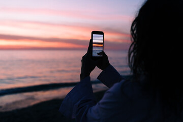 A Woman On the Beach Photographing the Sunset