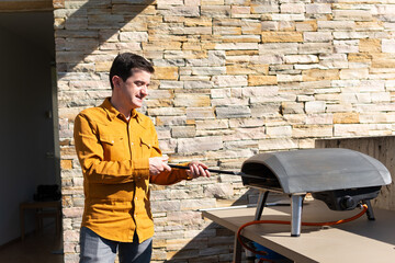 man in yellow shirt inserts spatula into a gas oven on his terrace contentedly enjoying the sun on his white skin. copy space