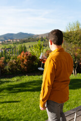 man drinks a glass of wine on the porch of his house while admiring the landscape of meadows, trees...
