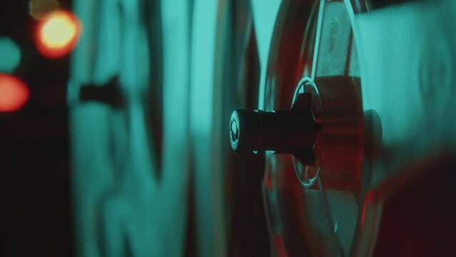 Close-up view of spinning reels of analog reel-to-reel tape recorder playing music in dark room with neon illumination and bokeh lights in defocused background