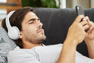 Man, headphones and phone for music on couch, relax and listen to song and scroll on social media. Male person, home and rest app for playlist or conversation, text and podcast audio for streaming