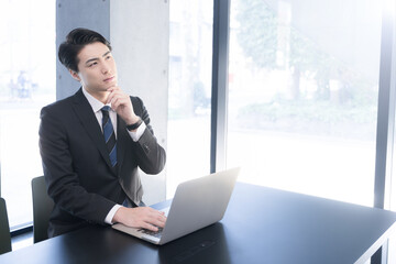 オフィスで働くビジネスマン　パソコンを見て考える困る迷う表情のイメージ　転職や採用にも