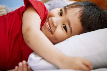 Smile, cute and boy child on bed playing and having fun at home with positive, good and happy...