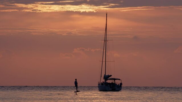 Silhouette of man riding an electric surf hydrofoil while having fun on water on vacation on sea voyage on sailing boat.