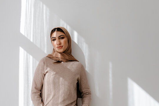 Smiling woman in hijab leaning on wall in studio
