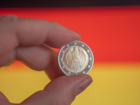Hand Holding a Euro Coin Over German Flag
