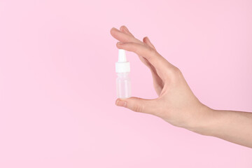 Woman with bottle of medical drops on pink background, closeup