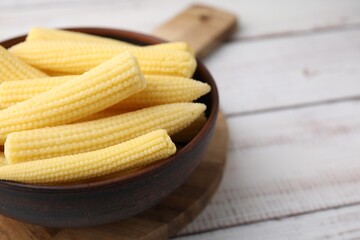 Tasty fresh yellow baby corns in bowl on white wooden table, closeup. Space for text