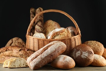 Wicker basket with different types of fresh bread on wooden table - Powered by Adobe