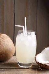 Tuinposter Glass of coconut water, ice cubes and nuts on wooden table © New Africa