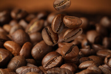 Roasted coffee beans falling on heap against brown background, closeup