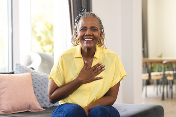African American senior woman sitting at home, laughing, hand on chest during a video call