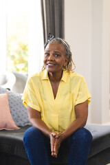A senior African American woman sitting at home, wearing a yellow shirt and jeans, on a video call