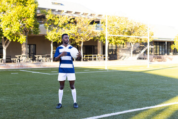 African American young male athlete holding rugby ball, wearing sportswear, copy space