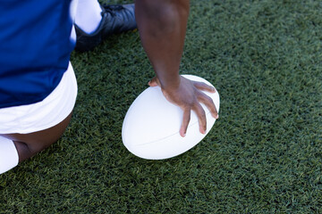 African American young male athlete holding a rugby ball on field outdoors, on grass, copy space