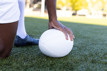 African American young male athlete holding white rugby ball on field outdoors on grass