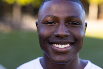 African American young male athlete smiling on field outdoors, wearing a white shirt, copy space