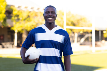 African American young male athlete holding a rugby ball, smiling at the camera, with copy space